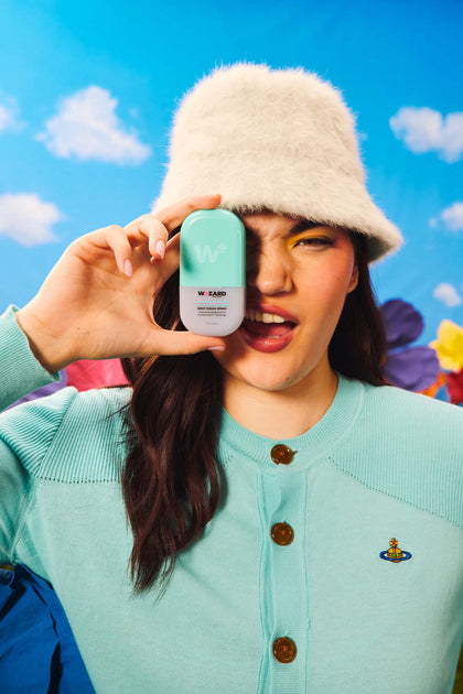 Person holding a product against a colorful background with flowers and a blue sky.