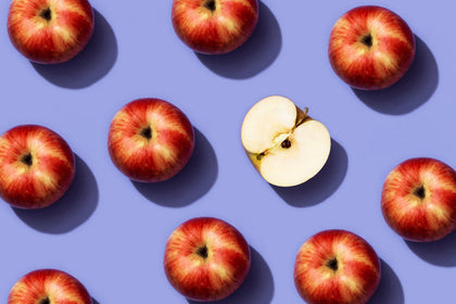 Pattern of red apples with one halved apple on a purple background
