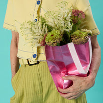 Person holding a pink bag with flowers against a teal background