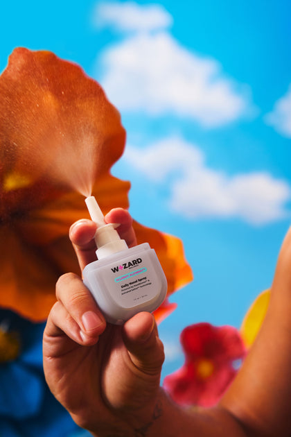 Hand holding the Wizard Nasal Spray with a blue sky and flowers in the background