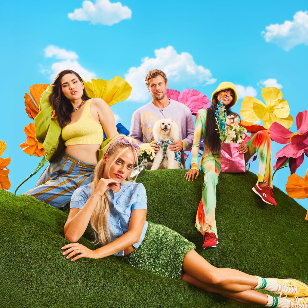 Four people sitting on a grassy hill with colorful flowers and a blue sky.