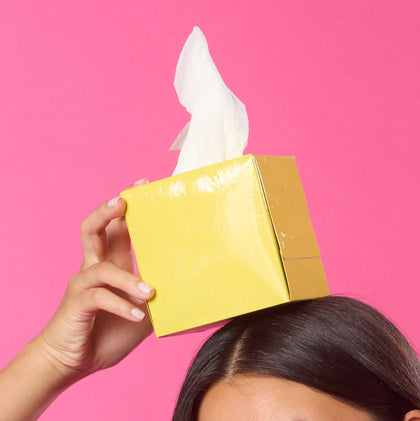 Person holding a yellow box of tissues with a pink background