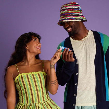 Two people standing against a purple background, holding the Wizard Happy Nose Nasal Stick.