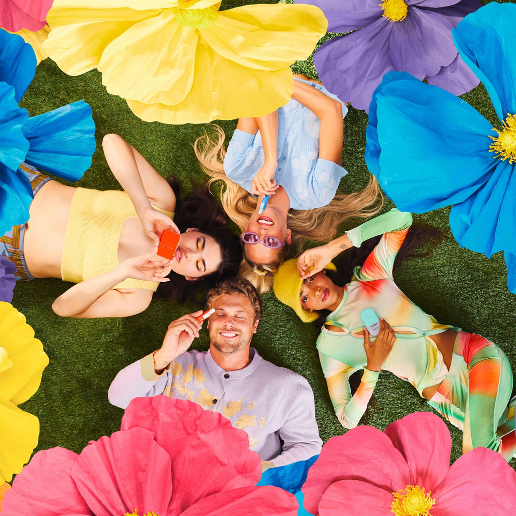 People lying on grass with Wizard Wellness products surrounded by large colorful flowers