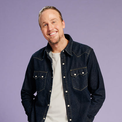 Man wearing a denim jacket over a white shirt on a purple background