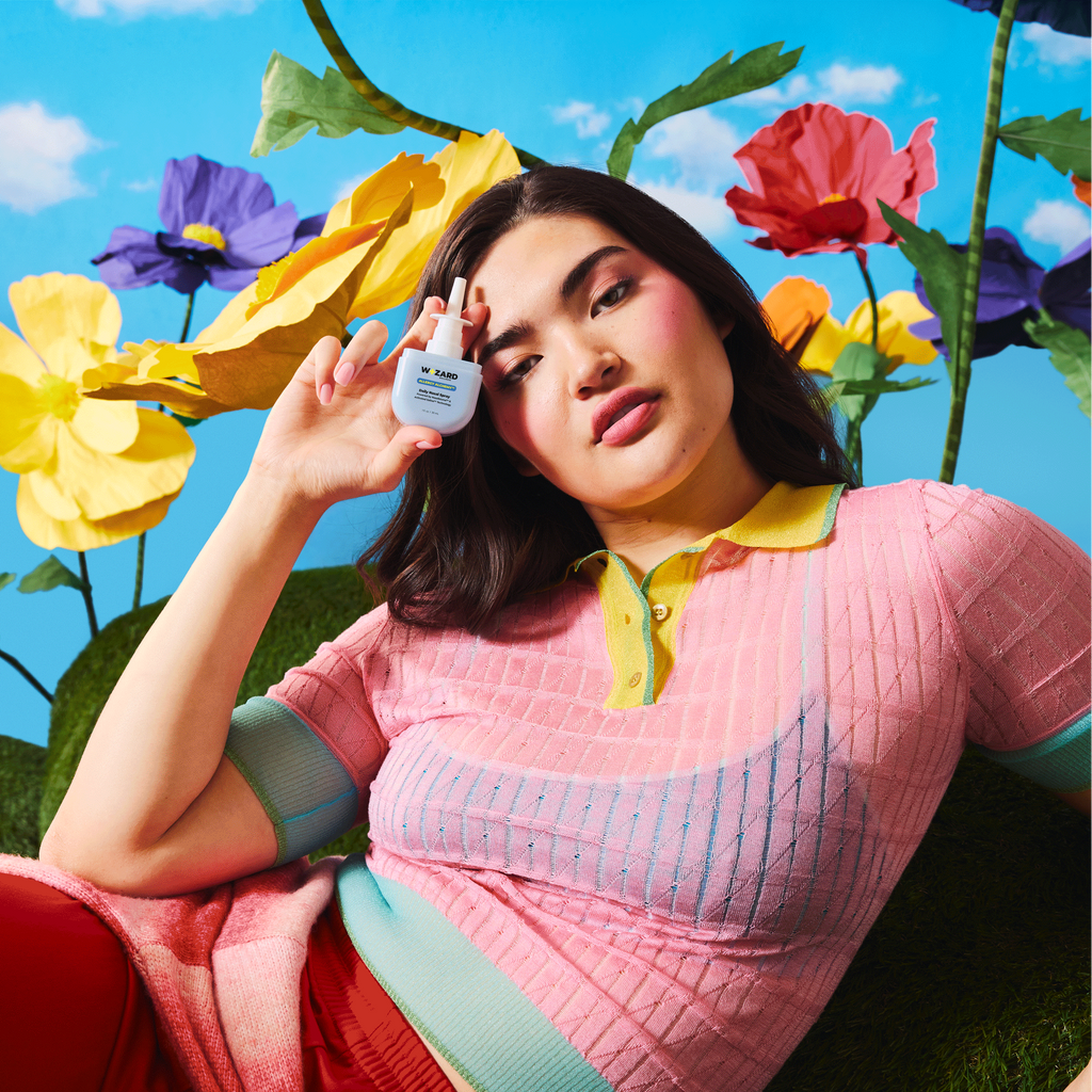 Woman holding the Wizard Nasal Spray with colorful flowers and sky in the background