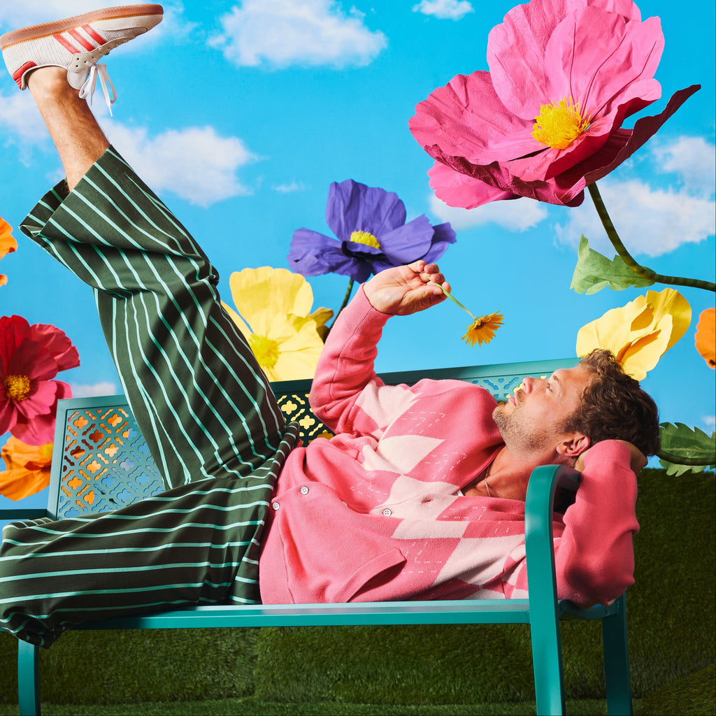 Person lying on a bench with large flowers and a blue sky in the background