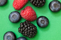 Assorted berries including raspberries and blackberries on a green background