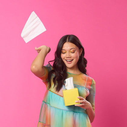 Woman in a colorful dress holding tissues against a pink background